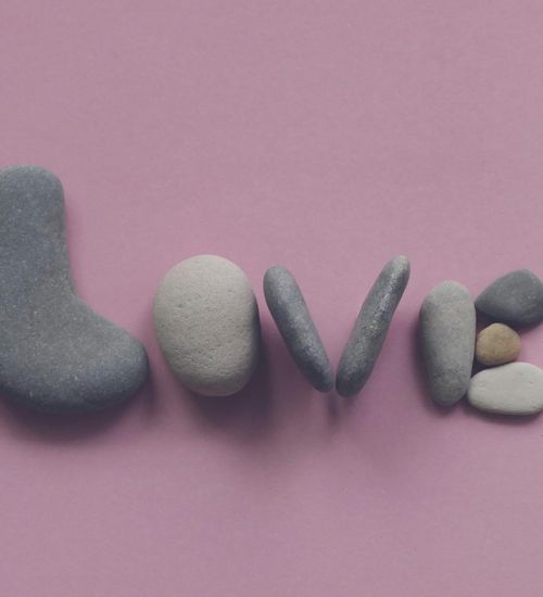 A balanced stack of smooth stones with a soft pink background.